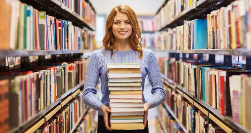 woman in library holding pile of books